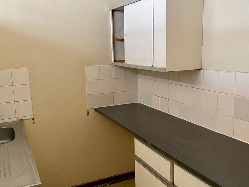 A compact kitchen featuring basic cabinetry, a laminate countertop, stainless steel sink, and an electric stove with tiled splashback.