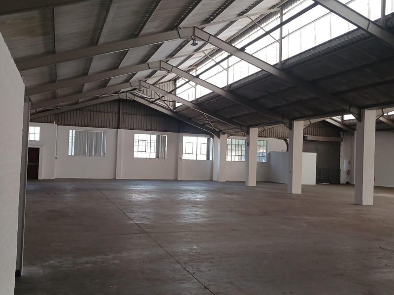 Spacious industrial warehouse unit featuring high ceilings, exposed steel trusses, concrete flooring, and ample natural light through clerestory windows.