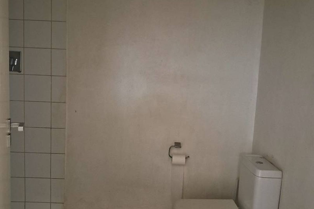 A basic bathroom featuring a standard toilet and a tiled shower area, requiring cosmetic updates and maintenance to improve its overall condition.