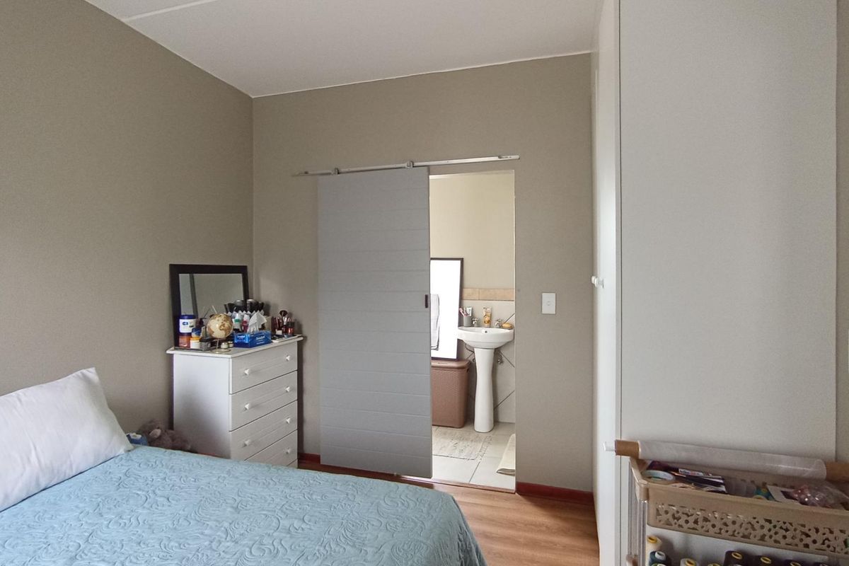 A bedroom featuring laminate flooring, a built-in wardrobe, and a sliding barn door providing access to an en-suite bathroom with a pedestal basin.