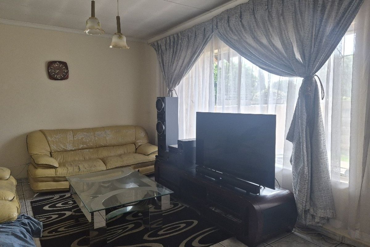 A living room featuring tiled flooring, pendant lighting, and a large window with curtains, providing a functional and well-lit space.