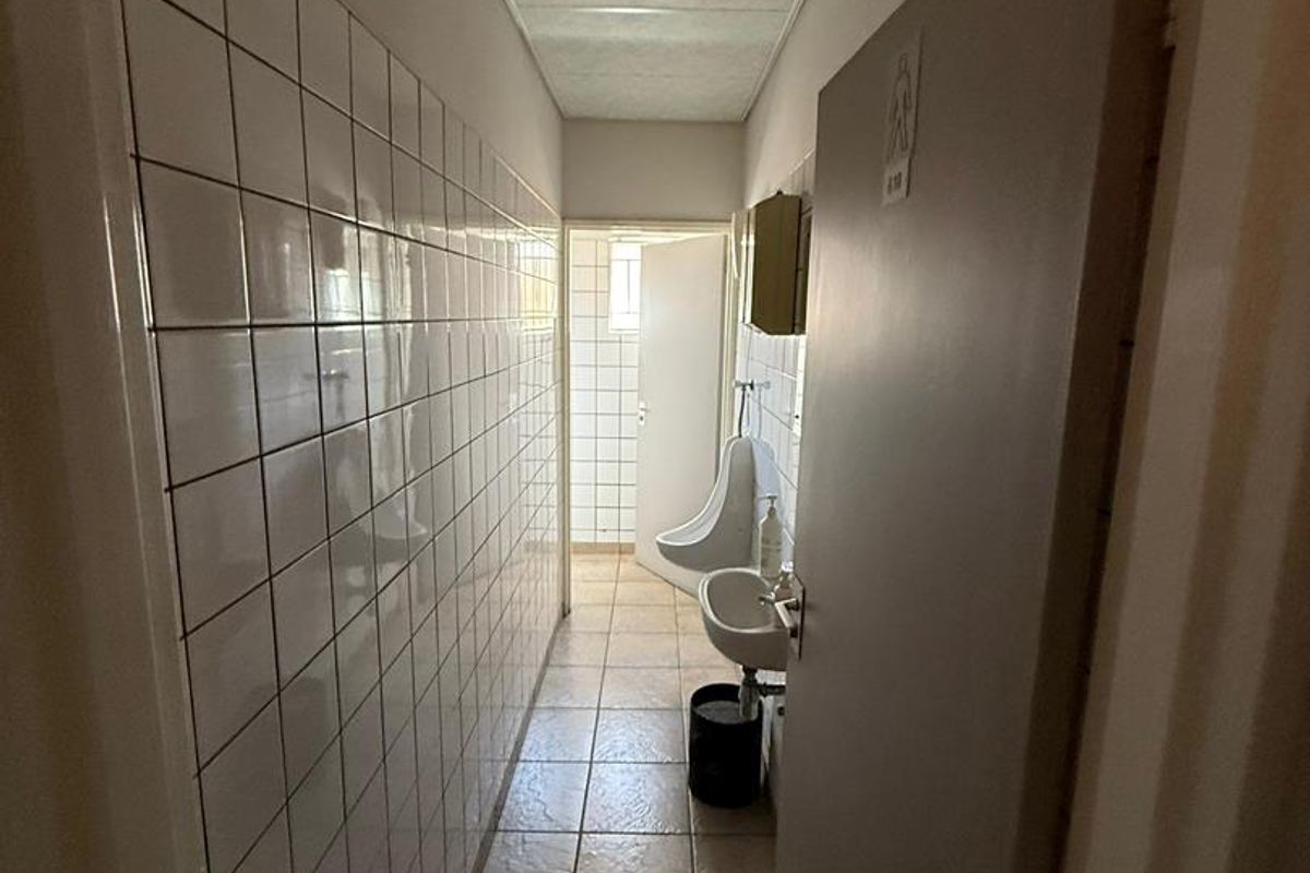 A functional office restroom facility featuring a wall-mounted urinal, a small hand basin, and tiled wall and floor finishes.