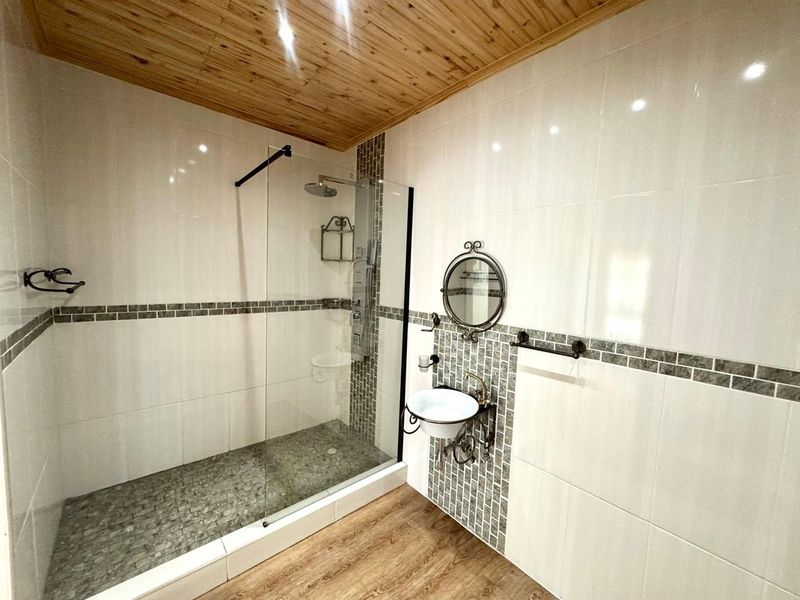 Modern bathroom featuring a walk-in shower with glass screen, pebble flooring, wall-mounted basin, and a warm timber ceiling finish.