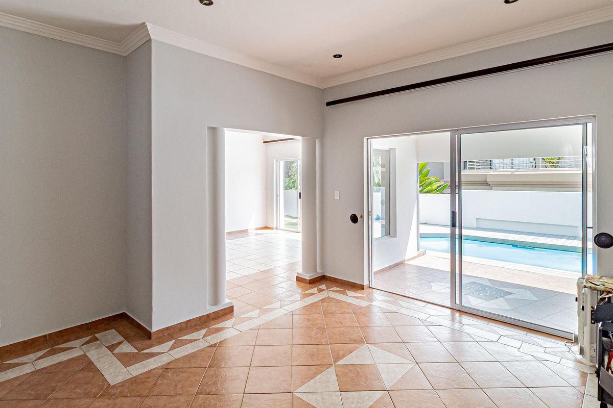 Spacious living area featuring tiled flooring, decorative columns, and large sliding glass doors providing direct access to the outdoor pool area.
