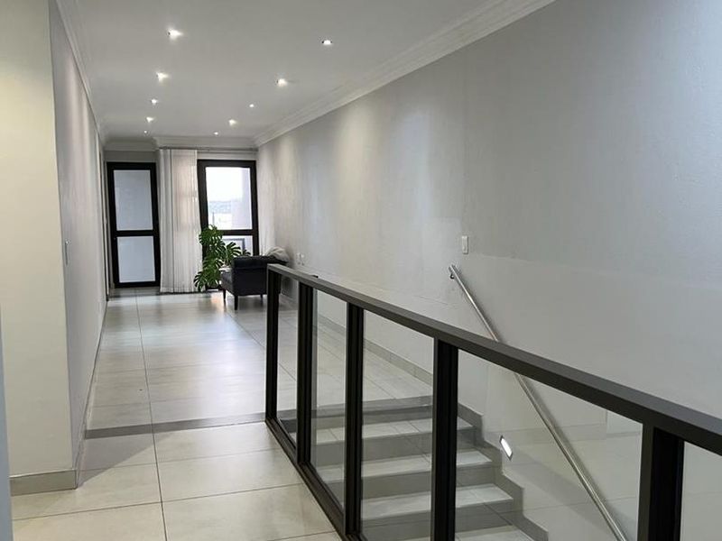 A bright, modern hallway featuring tiled flooring, recessed downlights, and a contemporary staircase with a glass balustrade.