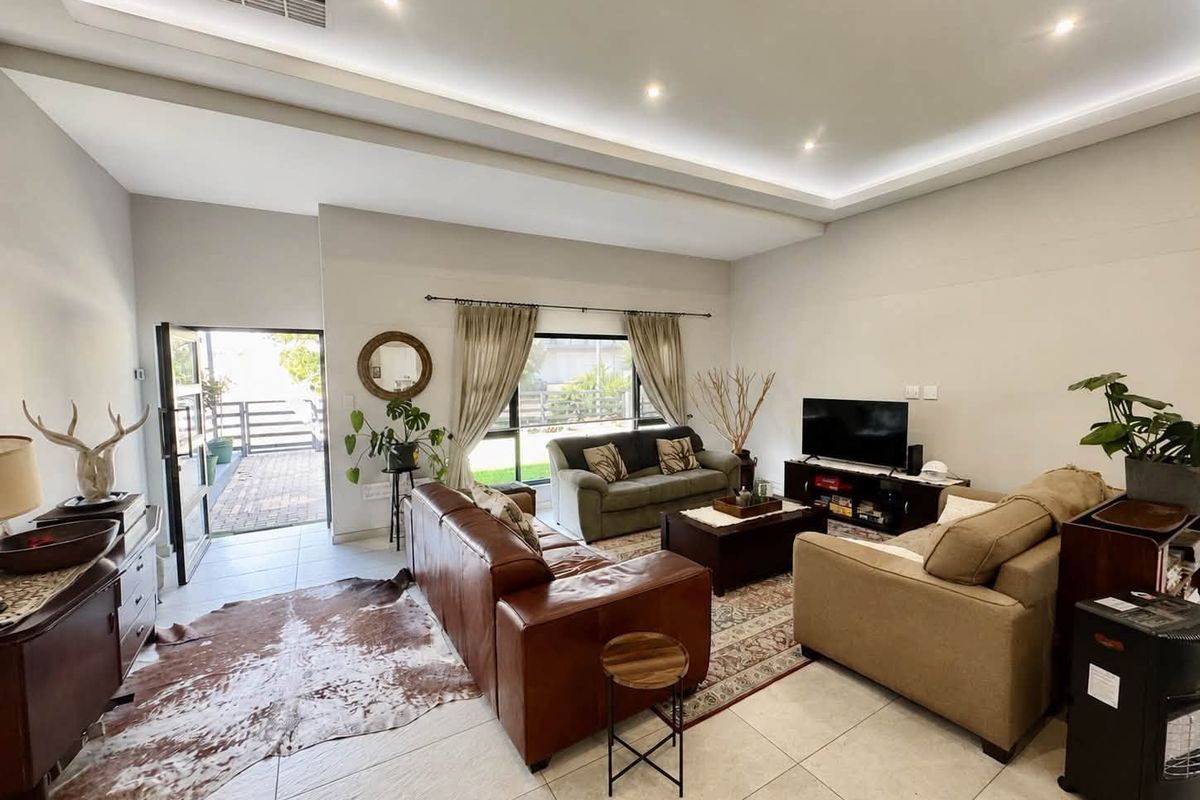 Spacious living room featuring a modern tray ceiling with recessed lighting, neutral tiled flooring, and direct access to an outdoor patio area.