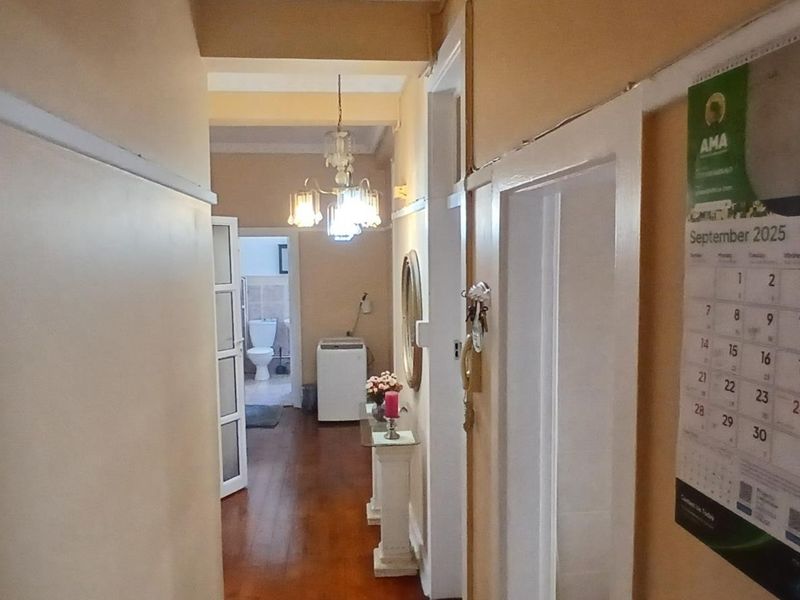 A view down a residential hallway featuring hardwood flooring and access to adjacent rooms, including a glimpse of a bathroom.