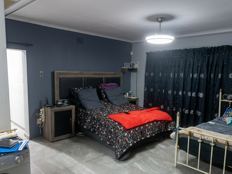A bedroom featuring tiled flooring, a ceiling fan with integrated lighting, and a dark accent wall.