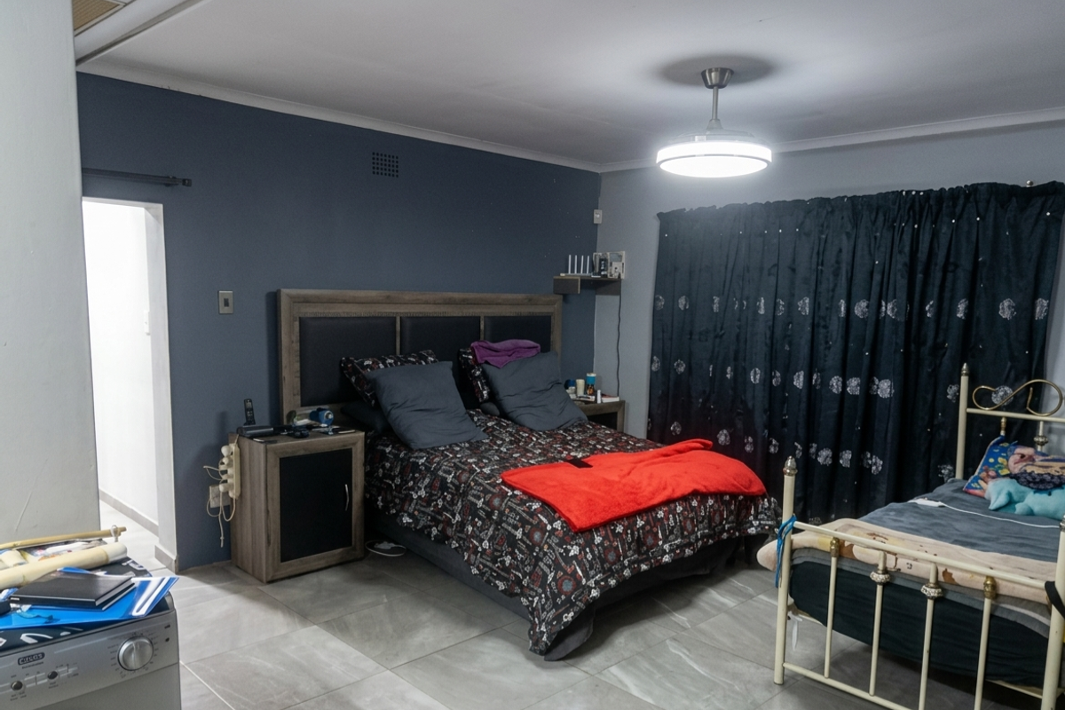 A bedroom featuring tiled flooring, a ceiling fan with integrated lighting, and a dark accent wall.