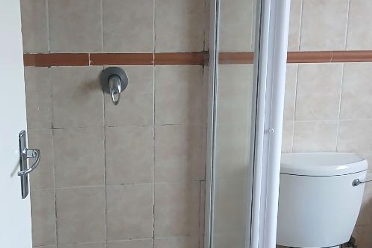 A functional bathroom featuring a shower enclosure with tiled walls and a standard toilet, requiring some maintenance to the tile grout.