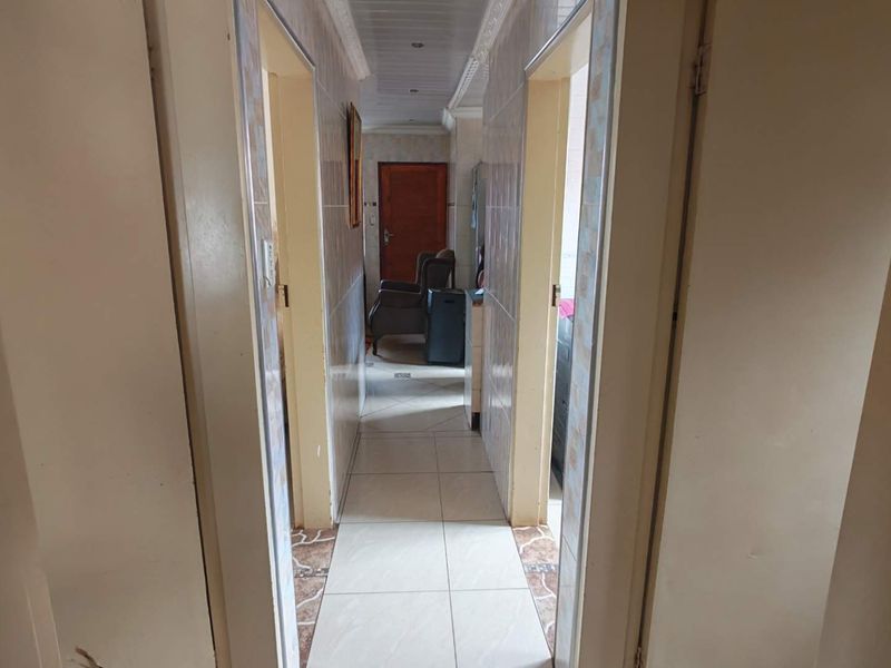 A narrow hallway featuring tiled flooring and wall cladding with recessed ceiling lighting, providing access to multiple rooms.
