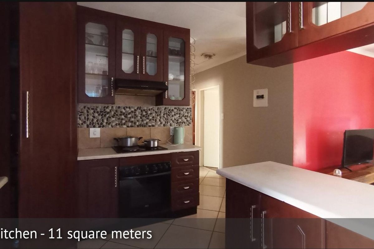 A functional kitchen featuring dark wood cabinetry, glass-fronted display units, a pebble mosaic backsplash, and a breakfast counter overlooking the living area.
