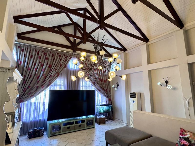 Spacious living room featuring high vaulted ceilings with exposed timber trusses, tiled flooring, and large windows with decorative curtains.