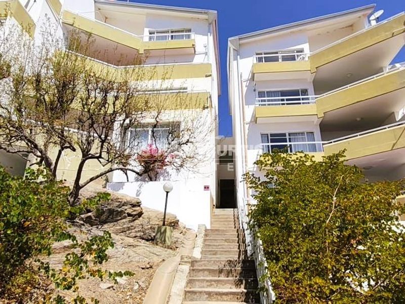 Exterior view of a multi-story apartment complex featuring concrete staircases, multiple balconies, and satellite dish installations.