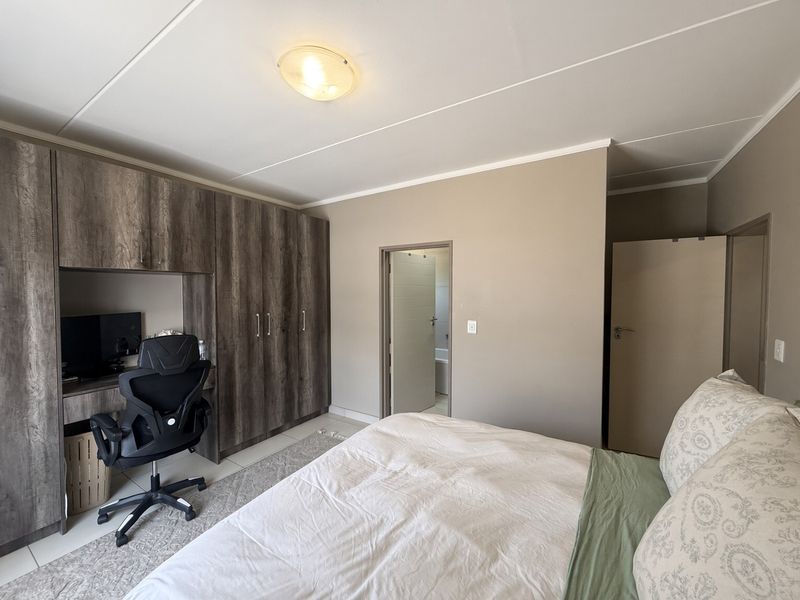 A well-maintained bedroom featuring built-in cupboards, an integrated desk workspace, and neutral wall finishes with direct access to an en-suite bathroom.