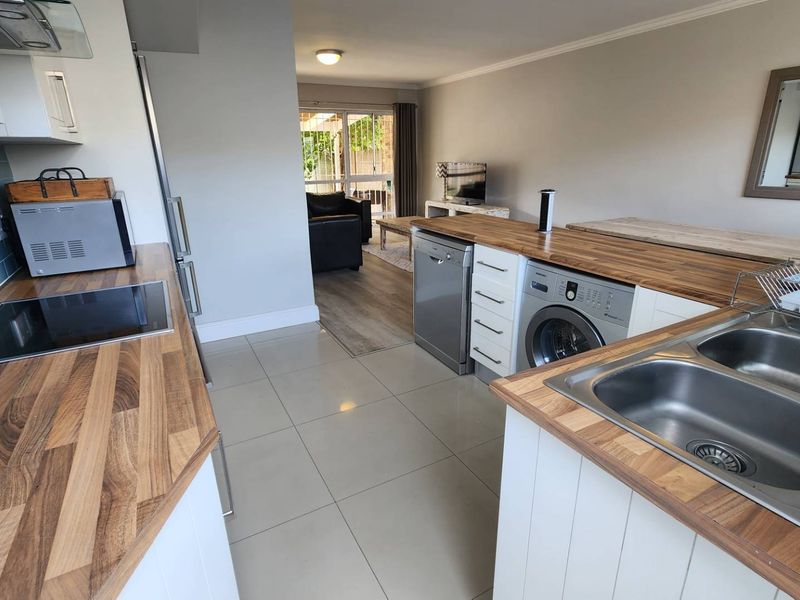 Open-plan kitchen and living area featuring wood-look countertops, modern cabinetry, tiled flooring, and direct access to an outdoor patio space.