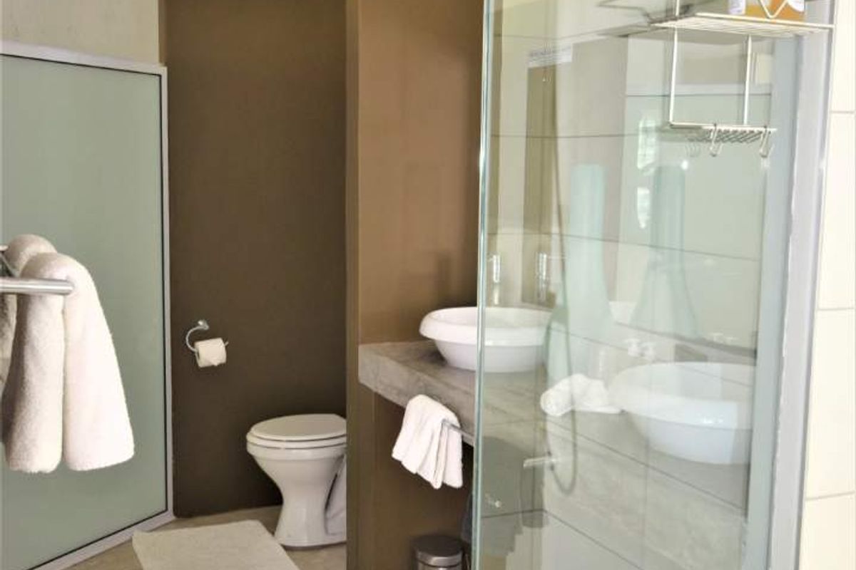 A bathroom featuring a glass-enclosed shower, dual vessel sinks on a concrete vanity, and a private toilet area with exposed ceiling beams.
