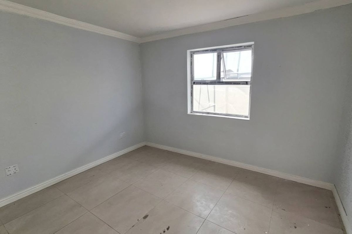 A clean, empty bedroom featuring neutral wall paint, tiled flooring, and a single window providing natural light.
