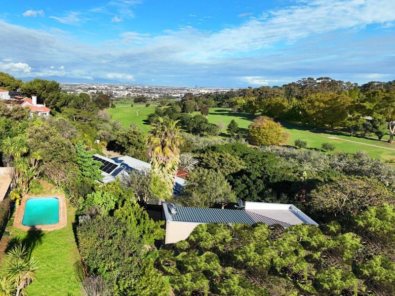 Aerial view of the property featuring a swimming pool, solar panels, and expansive green surroundings overlooking a golf course and city landscape.