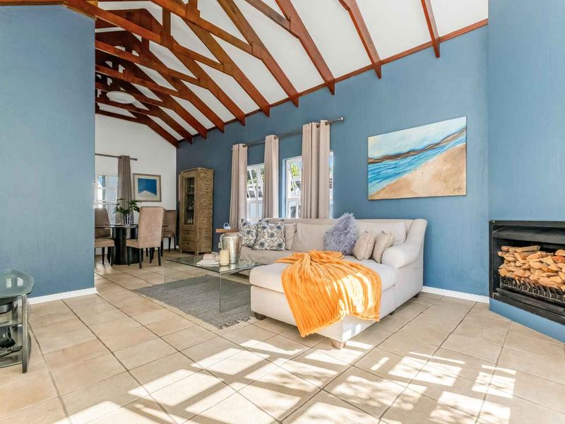 Spacious open-plan living and dining area featuring vaulted ceilings with exposed timber rafters, tiled flooring, and a cozy built-in fireplace.