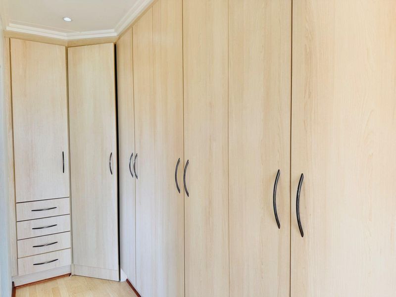 A bedroom featuring extensive light wood-finish built-in cupboards with integrated drawer storage and modern black handles.