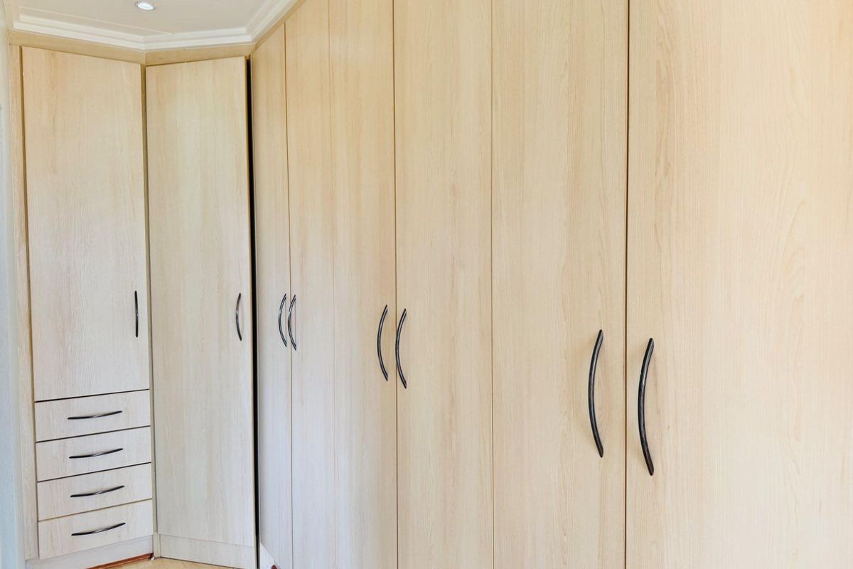 A bedroom featuring extensive light wood-finish built-in cupboards with integrated drawer storage and modern black handles.