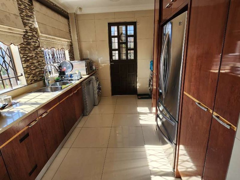 A functional kitchen featuring extensive wood-finish cabinetry, tiled flooring, a stainless steel sink, and a built-in refrigerator with ample natural light.