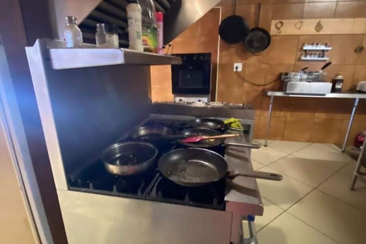 A commercial-style kitchen featuring a large stainless steel gas range, extractor hood, and tiled wall finishes, suitable for high-volume food preparation.