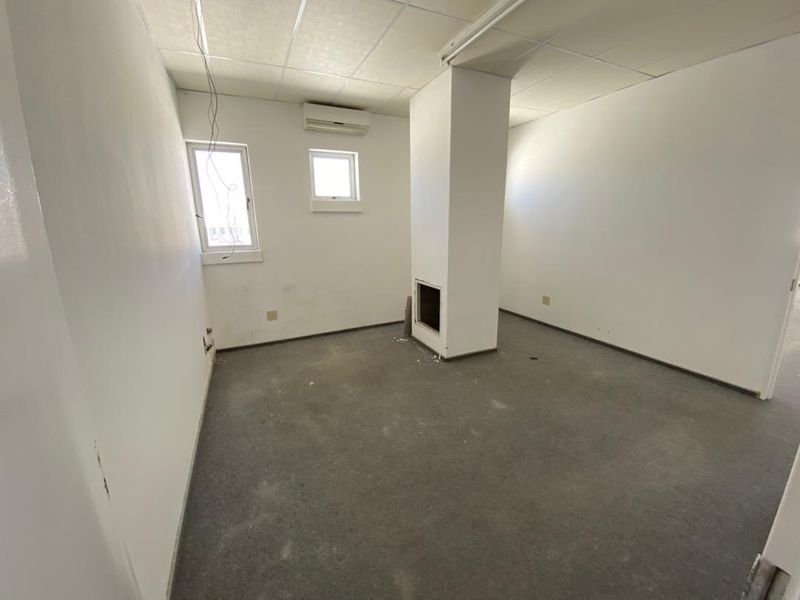 An empty office space featuring a suspended ceiling, wall-mounted air conditioning, and a central structural column, requiring cosmetic updates to the flooring and walls.