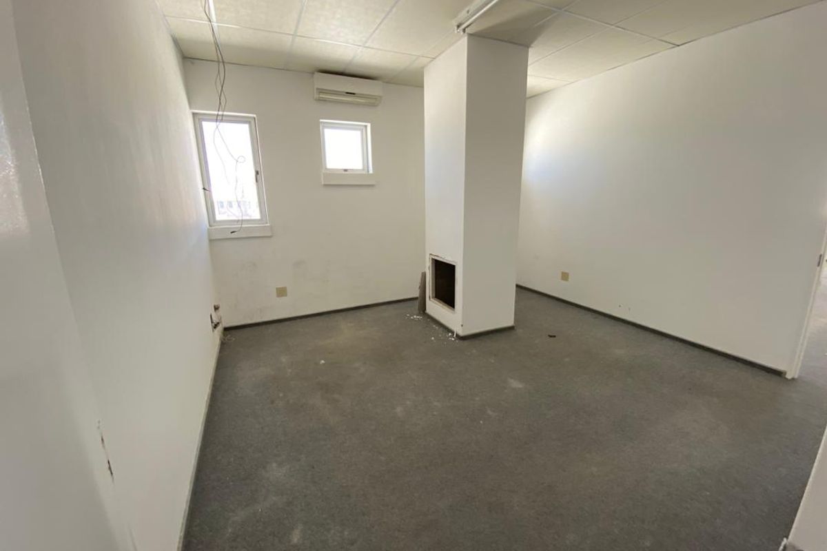 An empty office space featuring a suspended ceiling, wall-mounted air conditioning, and a central structural column, requiring cosmetic updates to the flooring and walls.