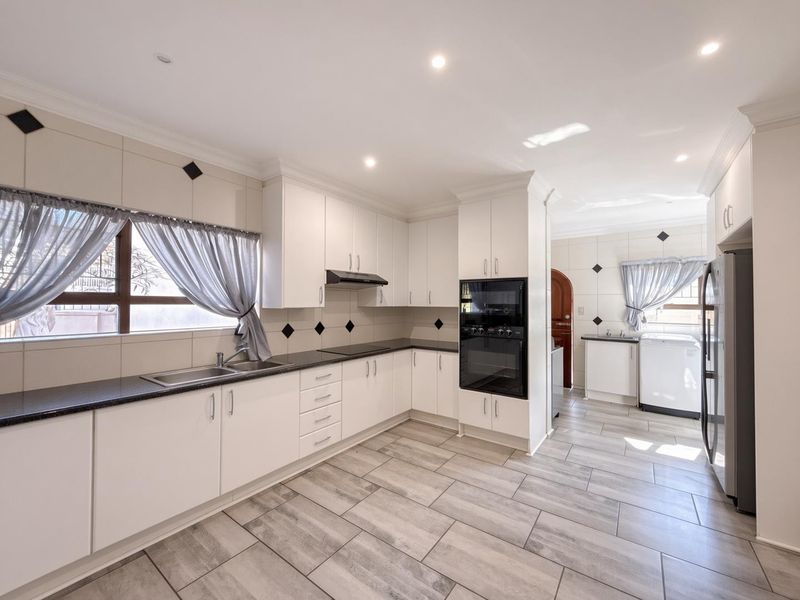A well-maintained kitchen featuring white cabinetry, dark countertops, built-in wall ovens, and tiled flooring, with an adjacent laundry area.
