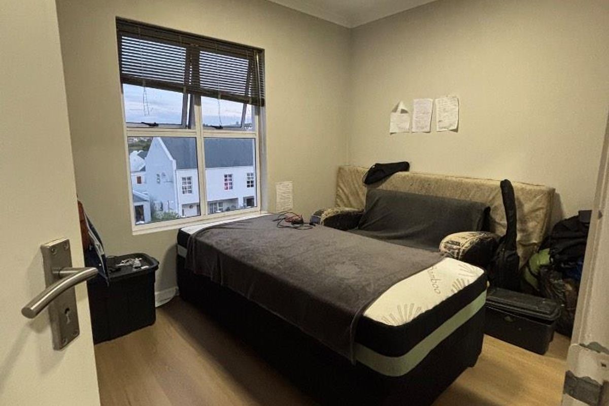 A functional bedroom featuring laminate flooring, a window with integrated blinds, and a ceiling light fixture, offering a neutral space for personalization.