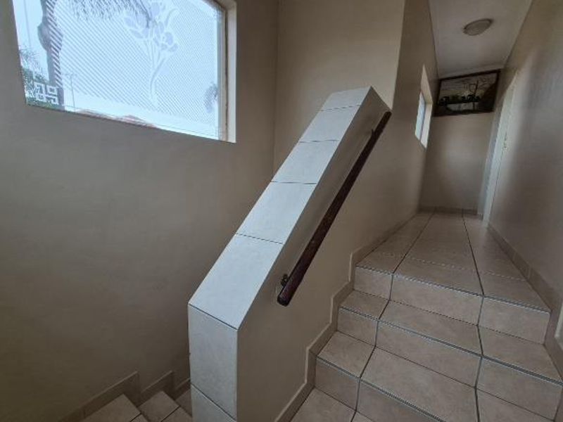 A tiled staircase featuring a tiled balustrade with a wooden handrail and a frosted glass window, providing a clean and functional transition space.