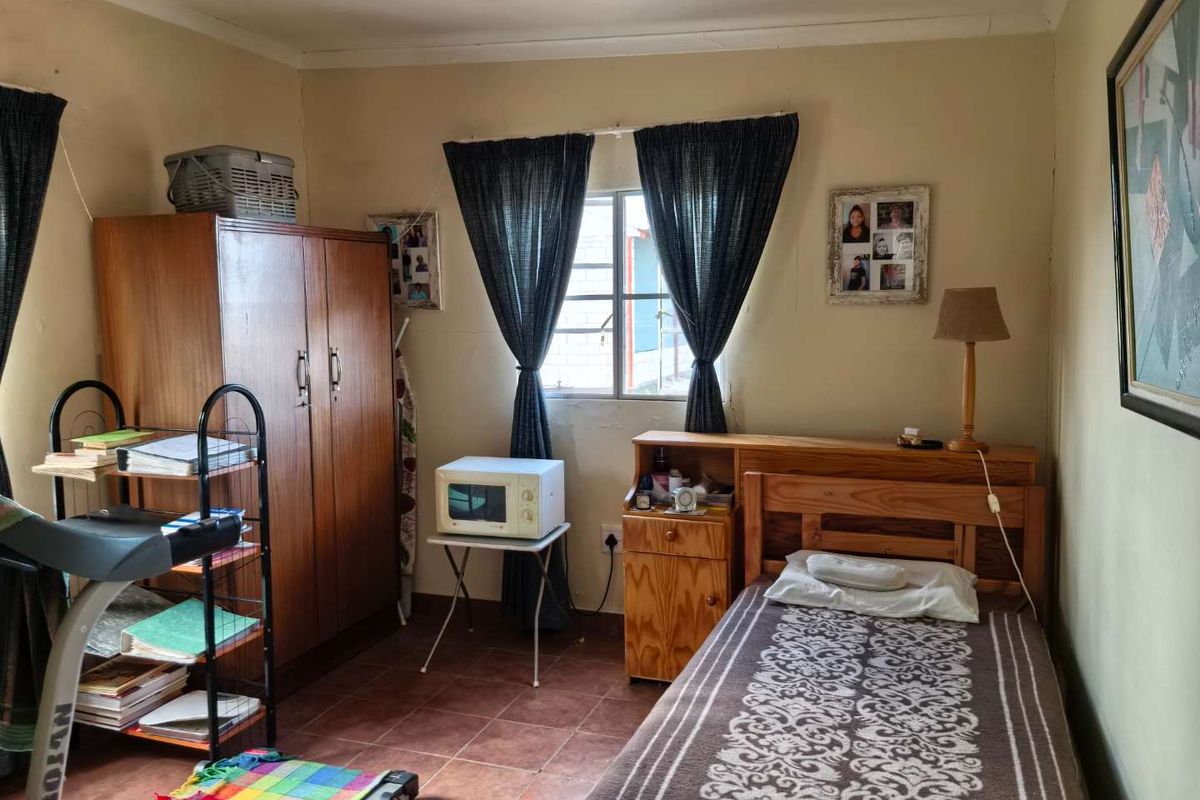 A compact bedroom featuring tiled flooring and a window with security bars, requiring cosmetic updates to improve the overall condition of the space.