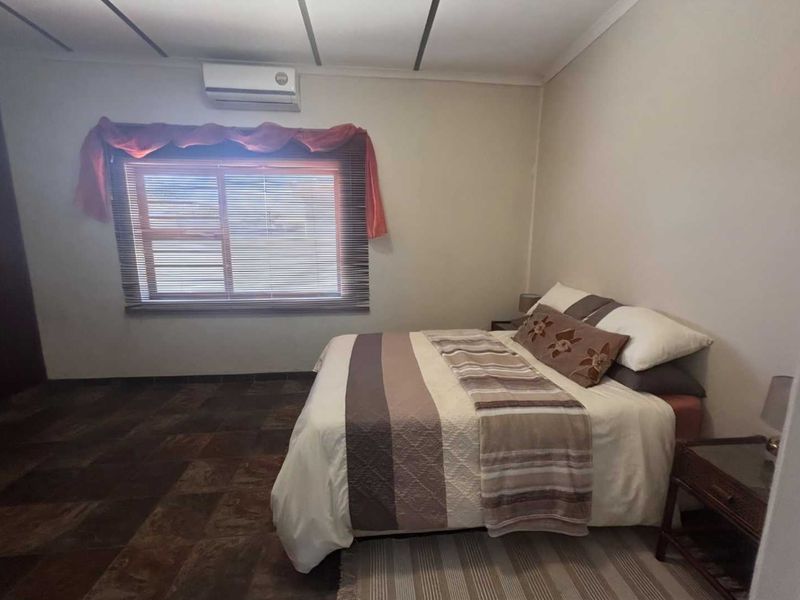 A bedroom featuring tiled flooring, a wall-mounted split-system air conditioner, and a built-in cupboard.