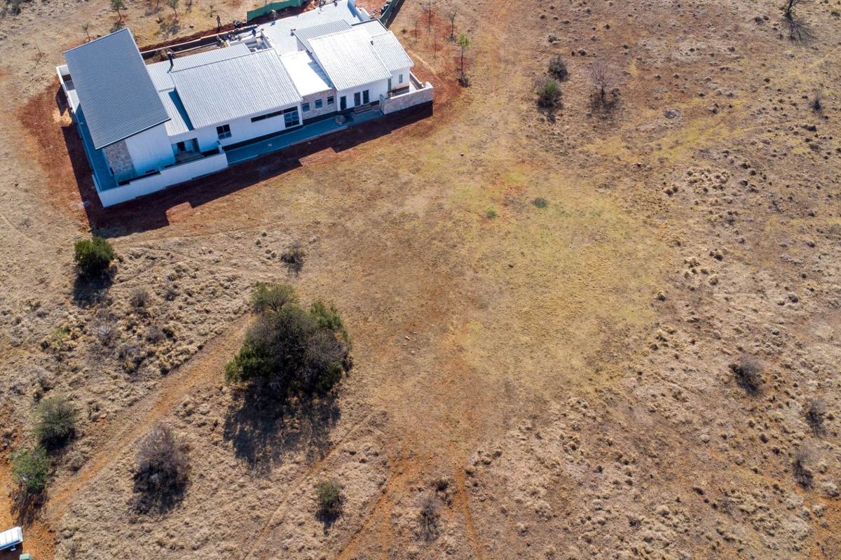 Aerial view of a modern residential property situated on a large, open plot of vacant land.