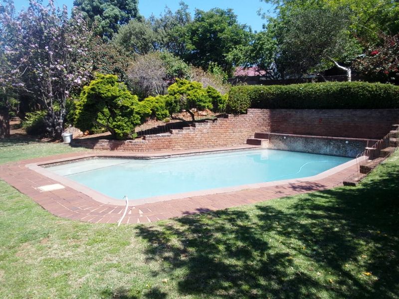 A private swimming pool area featuring a brick retaining wall and established garden surroundings, offering a tranquil outdoor space.