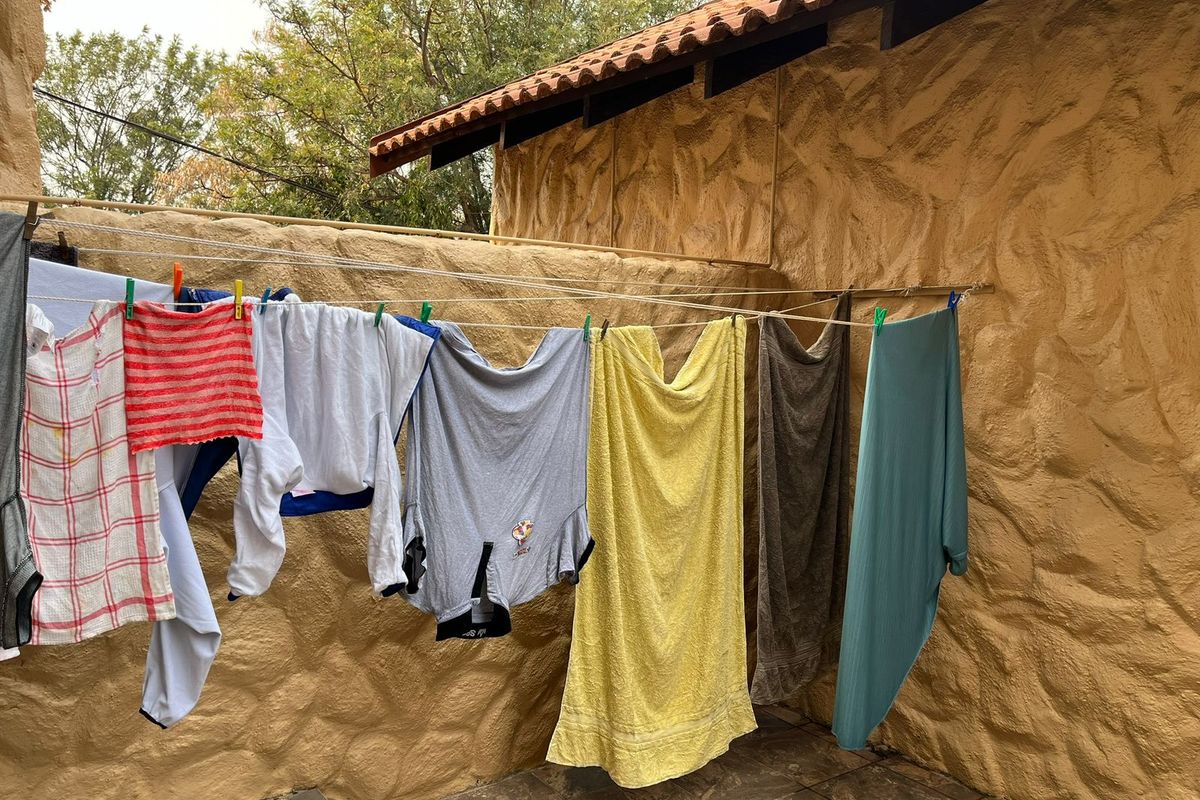 A rear exterior area featuring textured stone walls, tiled roofing, and paved flooring, currently utilized as a laundry drying space.