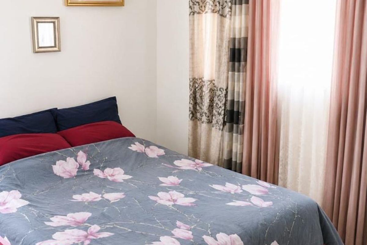 A well-lit bedroom featuring neutral wall finishes and floor-to-ceiling window treatments.
