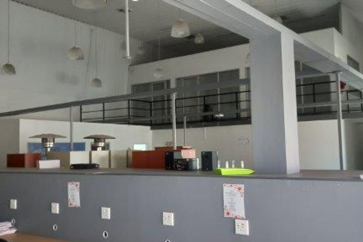 Spacious open-plan commercial area featuring a mezzanine level with metal railings, high ceilings, and integrated electrical infrastructure along the partition wall.