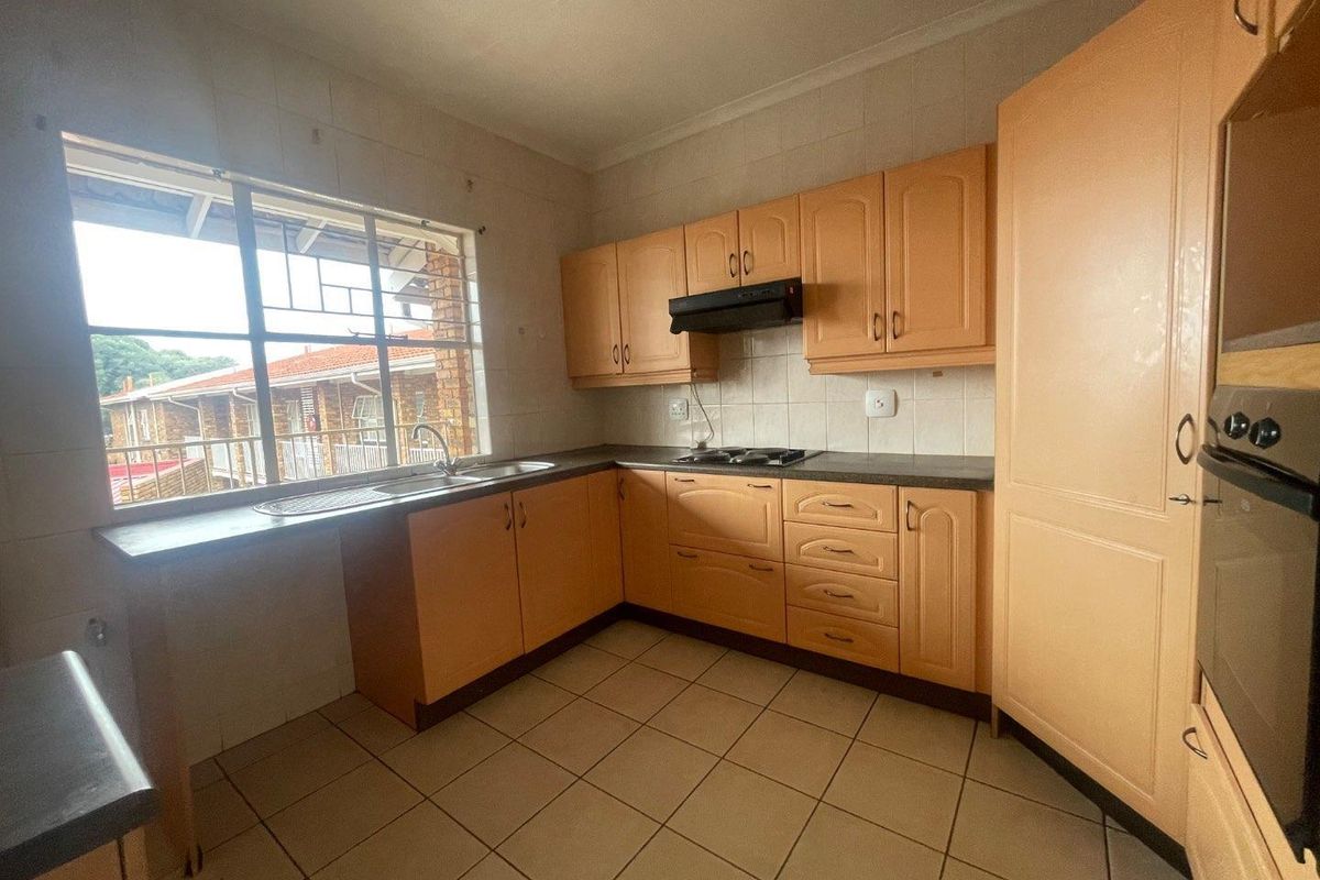 A functional kitchen featuring laminate cabinetry, built-in oven, hob, extractor fan, and tiled flooring, offering a practical layout with natural light.