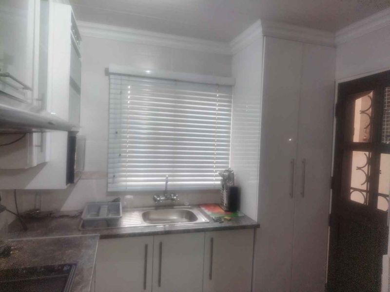 A functional kitchen area featuring white built-in cabinetry, a stainless steel sink, tiled backsplash, and venetian blinds over the window.