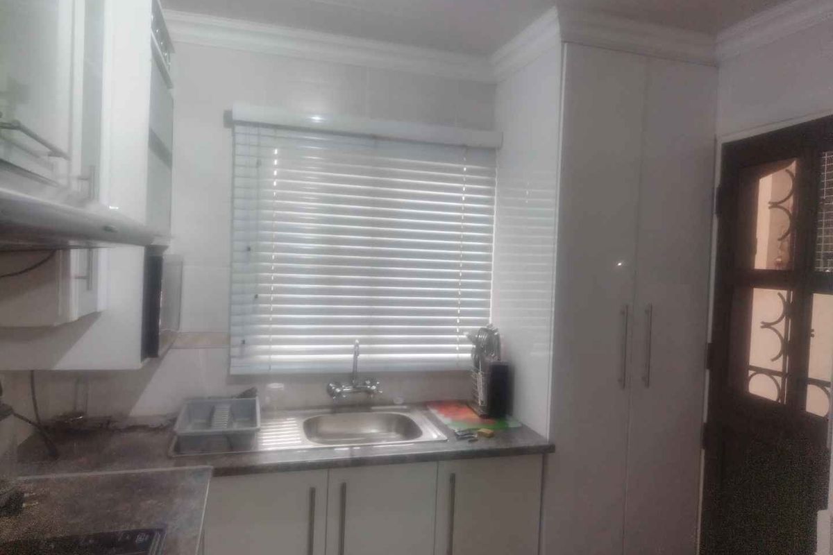 A functional kitchen area featuring white built-in cabinetry, a stainless steel sink, tiled backsplash, and venetian blinds over the window.