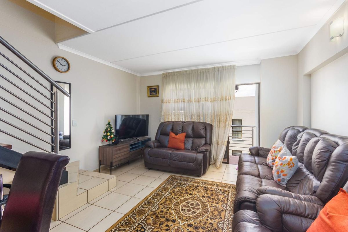 A living room featuring tiled flooring, a staircase with a metal railing, and a sliding glass door providing access to a balcony.