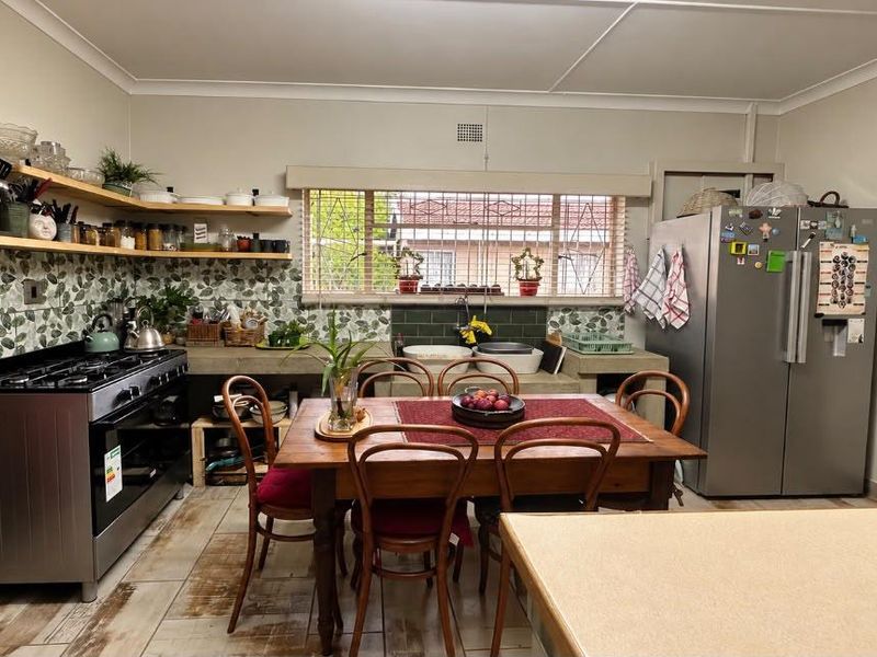 A functional kitchen featuring a gas stove, concrete countertops, double basin sink, and decorative tiled backsplash with open timber shelving.