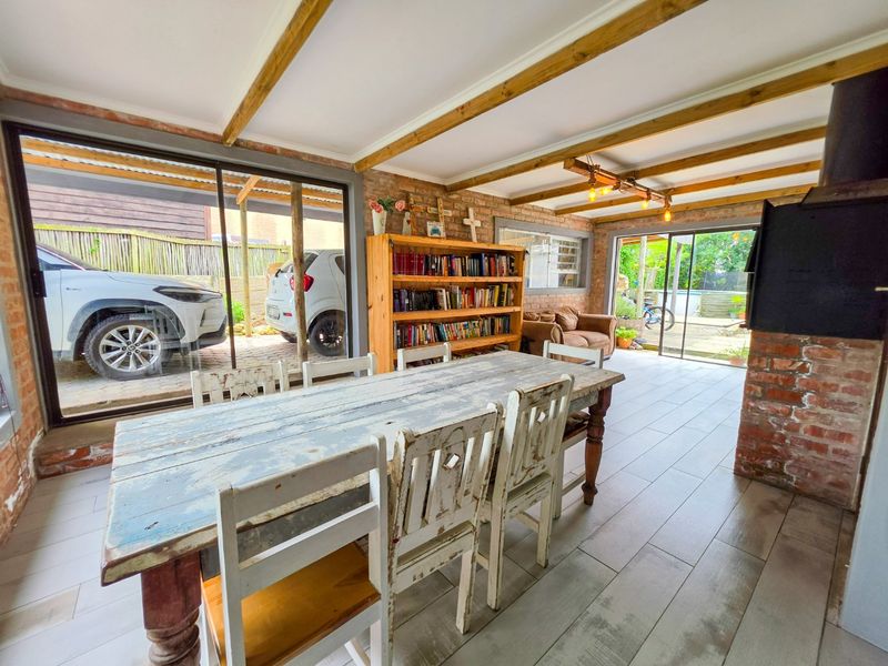 Spacious dining area featuring exposed brick walls, timber ceiling beams, tiled flooring, and a built-in fireplace with direct access to the outdoor area.