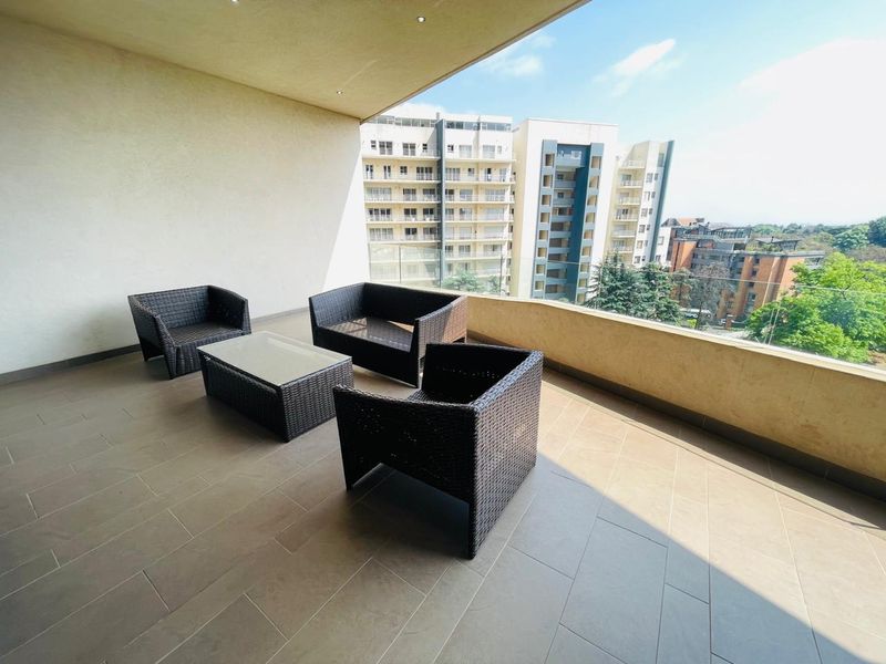 Spacious covered balcony featuring tiled flooring, recessed ceiling lights, and a modern glass balustrade with views of the surrounding apartment complex.
