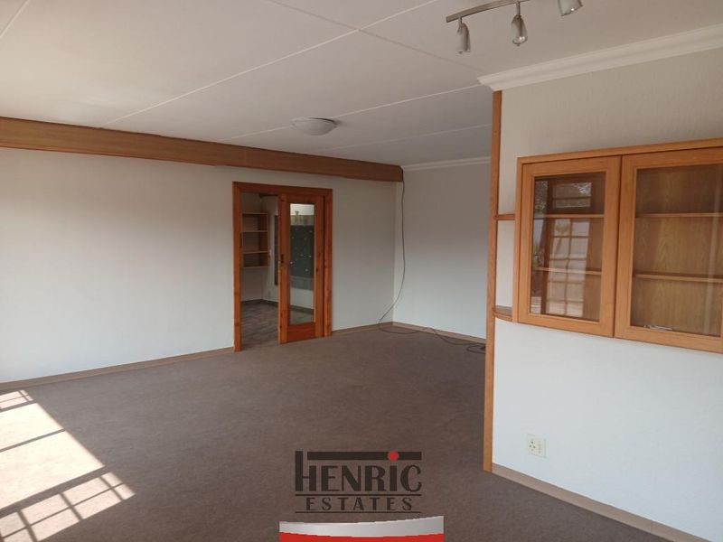 Spacious, empty living area featuring neutral walls, carpeted flooring, and built-in wooden cabinetry, providing a versatile blank canvas for interior design.