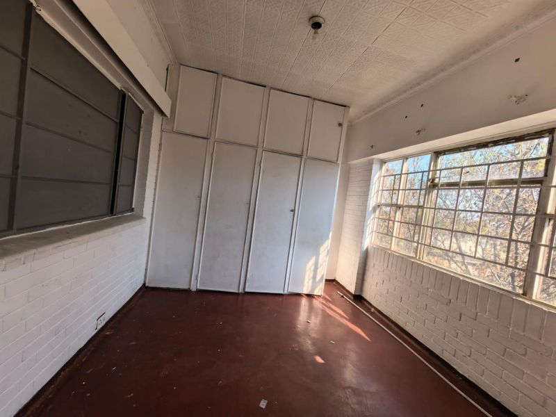 An empty bedroom featuring built-in cupboards, painted brick walls, and security bars on the windows, requiring cosmetic updates to improve its condition.