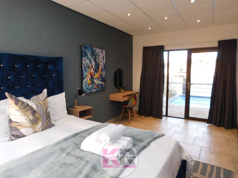 Spacious bedroom featuring tiled flooring, recessed ceiling lighting, and a sliding glass door providing direct access to the outdoor pool area.